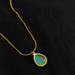 Emerald green teardrop pendant necklace with gold plated chain on black background