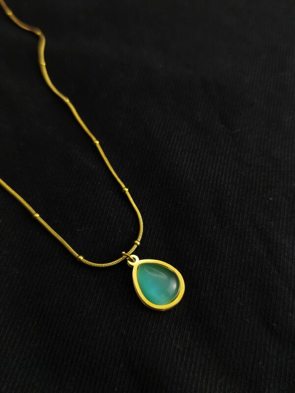 Emerald green teardrop pendant necklace with gold plated chain on black background